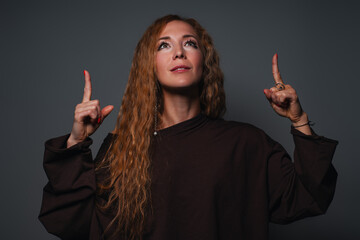 Young woman pointing fingers up, portrait on gray background
