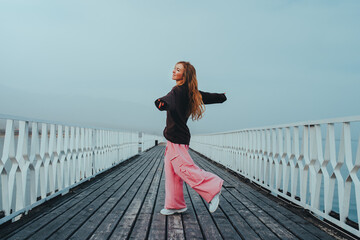 Young woman dancing on pier on lake shore on summer day