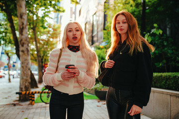Two young women friends with coffee walking on city street in summer Seoul