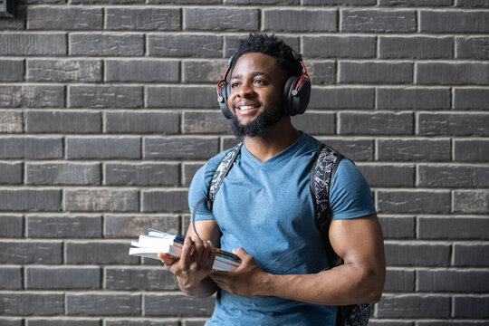 A young man happily wearing headphones while holding books, emphasizing relaxation and enjoyment in studying.