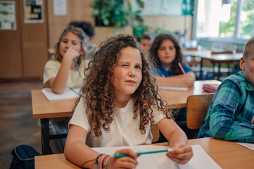 Curious girl winking and thinking during class at elementary school