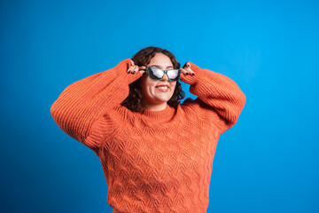 Plus size fashion model wearing sunglasses and orange sweater on blue background