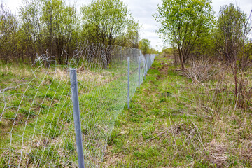 A mesh fence laid across an overgrown field