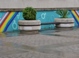 Betonblumentöpfe auf Platz vor Mauer mit Regenbogen