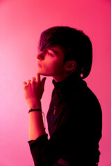 A young woman with short hair is standing in front of a pink background