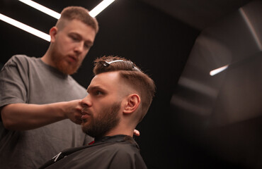 Barber gives a sharp modern haircut to a focused male client under geometric LED lighting in a...