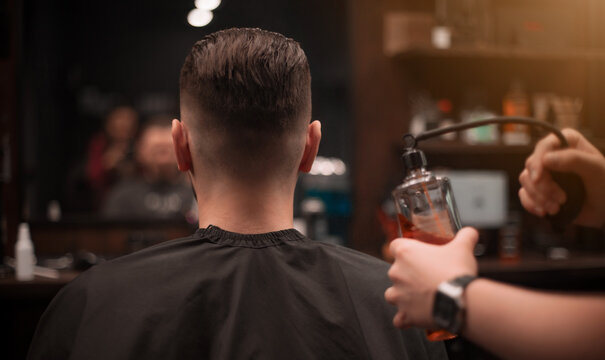 A male barber sprays disinfectant on a client's neck after a haircut in a modern barbershop. The focus is on the clean fade and hygienic grooming process..