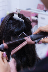 Fototapeta premium Detail of a woman's hands straightening a young woman's hair with a specialized flat iron inside a beauty salon in Neiva, Huila, Colombia. Beauty, hairstyle and hairstyling concepts