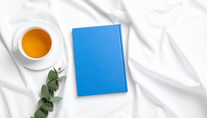 Blue Journal Beside Herbal Tea and Eucalyptus Leaves on White Fabric