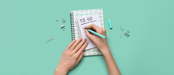 Female hands with to do list on turquoise background. Top view