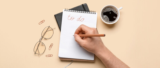 Male hand with to-do list, cup of coffee and eyeglasses on yellow background
