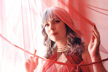 Eine hübsche Frau im roten Kleid schaut durch einen Vorhang