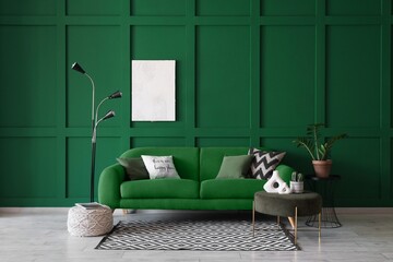Cozy sofa, pouf, coffee table, houseplant and floor lamp near green wall in room