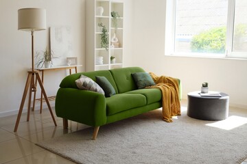 Cozy green sofa, pouf, shelving unit and floor lamp in interior of living room