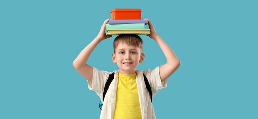 Cute little schoolboy holding books and lunchbox on blue background