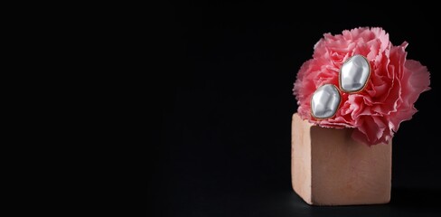 Decorative podium, beautiful flower and stylish pearl earrings on black background with space for text
