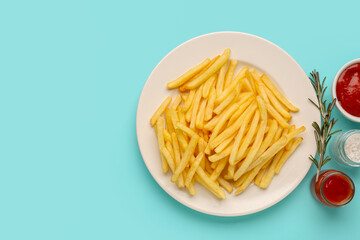 Plate with tasty french fries, ketchup and salt on light blue background