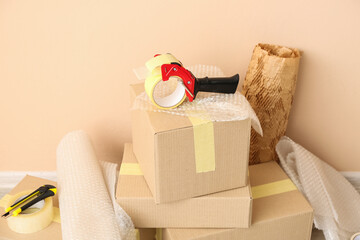 Packing tape dispenser, cardboard boxes and rolls of bubble wrap near beige wall