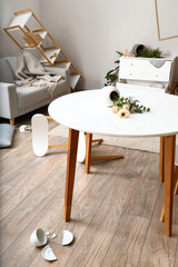 Dining table with fallen vase and flowers in messy room