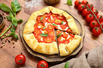 Board with tasty tomato galette and basil on wooden background