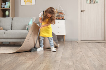 Cute little girl sweeping floor under carpet with broom at home