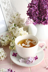 Cup of tea with lilac flowers and frame on pink tile near grunge white wall