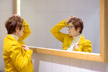 Portrait of an elderly woman in front of a mirror. A beautiful red-haired senior carefully examines her reflection in the mirror.