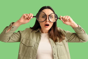 Shocked young woman with magnifiers on green background