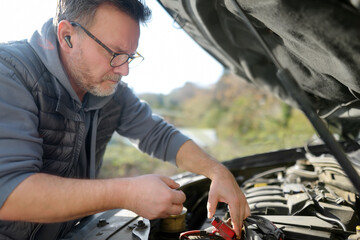 A middle-aged man repairs a car during a trip