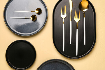 Clean black plates with golden cutlery on yellow table