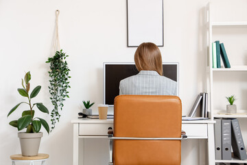 Young woman working with computer at table in office, back view