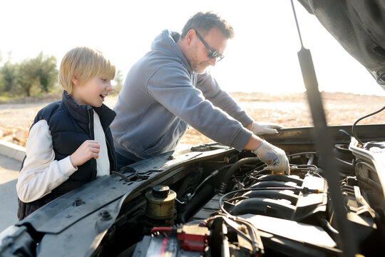 A middle-aged father and a preteen son work on a car during a road trip