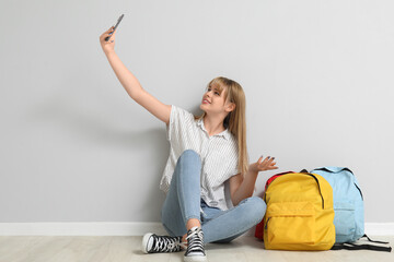 Female student with backpacks taking selfie near light wall