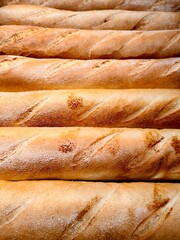 golden brown breadsticks are freshly baked and lined up on wooden board in bakery. warm aroma fills air, enticing customers to try delicious treats. close-up.