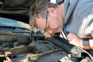 A middle-aged man repairs a car during a trip