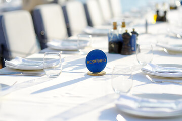 A row of empty plates on a long table with a white tablecloth. A table in a Mediterranean restaurant ready to serve a large group of visitors or tourists.
