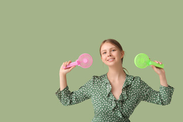 Beautiful young woman with handheld mini fans on green background