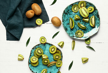 Plates with slices of fresh kiwi and leaves on white wooden background