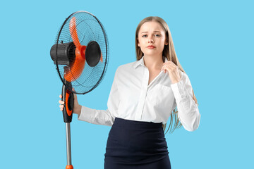 Sweaty young businesswoman with electric fan on blue background