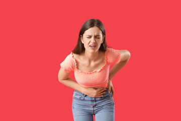 Young woman suffering from stomach ache on red background