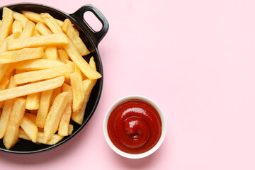 Black bowl with golden french fries and ketchup on pink background, closeup