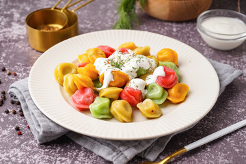 Plate of boiled colorful dumplings with sour cream and dill on dark background