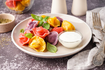 Plate of boiled colorful dumplings with basil and sour cream on dark table