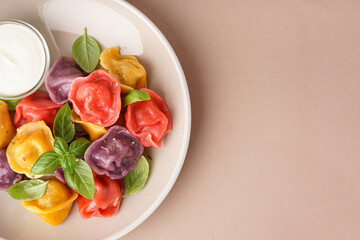 Plate of boiled colorful dumplings with basil and sour cream on beige background