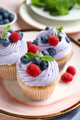 Plate of delicious cupcakes with blueberries, raspberries and mint on table