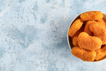 Bowl with tasty nuggets on blue background
