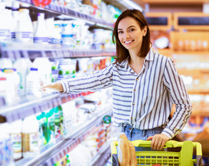 Retail Concept. Smiling Young Lady Standing With Shopping Trolley Cart Near The Shelves In Grocery...