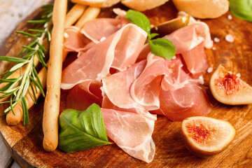 Plate with slices of tasty prosciutto, basil, Italian Grissini and figs on table