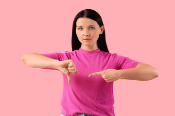 Young woman showing dislike on pink background