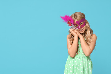 Funny little girl wearing carnival mask on blue background
